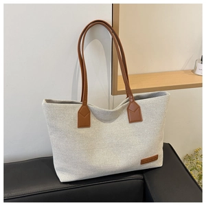 Close-up of cream canvas tote bag showing textured weave and brown leather fashion tag