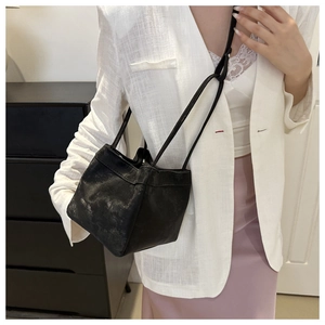 Detail of a minimalist black bucket bag with slim strap on a white linen suit
