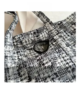 Detailed close-up of a black and white tweed tote bag with a functional exterior pocket