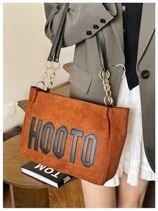 Detail of brown faux suede tote bag featuring HOOTO logo and golden chain strap