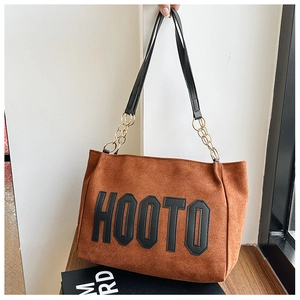 Detailed close-up of brown suede tote bag with bold HOOTO letter patches and gold chains