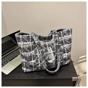 Detail of checkered tweed tote bag showing woven texture on a desk with a laptop