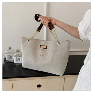 Close-up of canvas tote bag with brown leather straps and gold deer charm detail