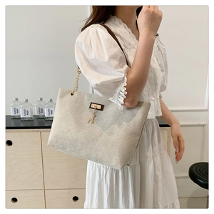 Detail of beige woven tote bag featuring gold deer charm and chain leather shoulder strap