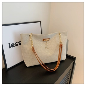 Close-up of beige canvas tote with brown leather straps and gold deer pendant charm