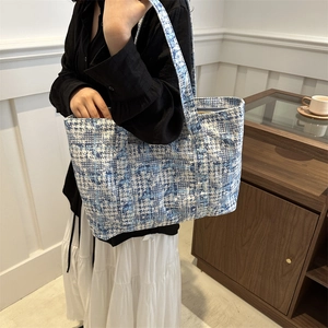 Fashionable blue plaid tote bag with wide shoulder strap carried by model in a modern room