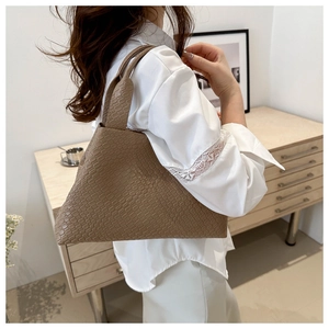 Detalle del bolso tote marrón con textura trenzada llevado al hombro por una modelo real