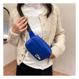 Detail of bright blue nylon crossbody bag with fashion patch worn by a model