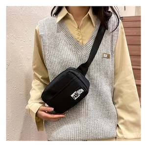 Detail of a black nylon crossbody bag with fashion patch and multiple zip pockets on a model