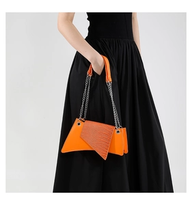 Detail of an orange crocodile pattern shoulder bag with a silver metal chain strap