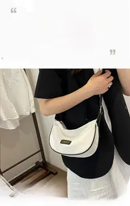 Détail du sac demi-lune blanc avec bordure contrastée noire et plaque logo moderne
