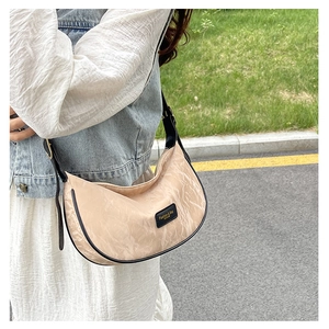 Détail du sac demi-lune beige avec bordure noire et écusson de marque sur la texture