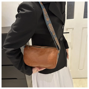 Gros plan sur un sac à bandoulière marron vintage avec large sangle brodée ethnique
