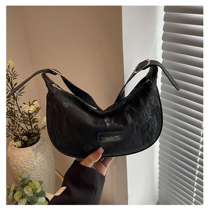 Détail d'un sac demi-lune noir à texture plissée et étiquette de marque dorée