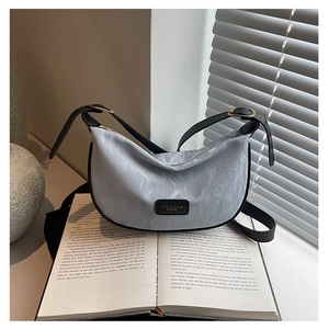 Détail du sac demi-lune bleu clair marbré avec boucle dorée sur un livre ouvert