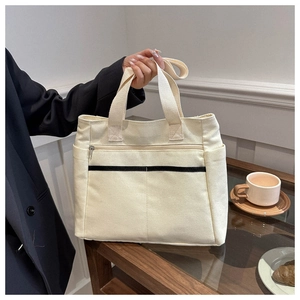 Detail view of cream canvas tote bag with side pocket and contrast black strap accent