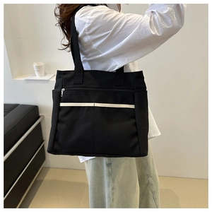 Close-up of black canvas tote bag with white stripe and metal zipper pocket detail