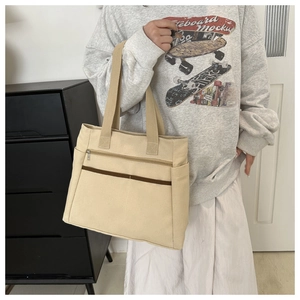 Detail view of large beige canvas tote bag with front zipper pocket and wide straps