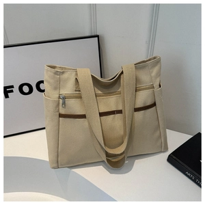 Detail of beige canvas tote bag showing front metal zipper pocket and brown ribbon straps