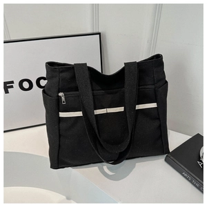 Detail of black canvas tote bag showing outer zipper pocket and striped design