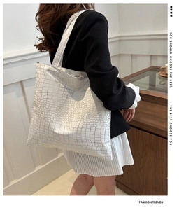 Model wearing a large white and gold crocodile pattern tote bag in a minimalist room