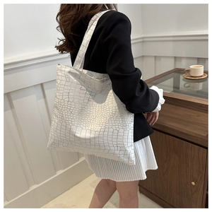 Detail of white crocodile embossed tote bag with gold texture on a female model