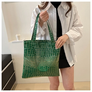 Detail of green crocodile texture tote bag with metallic accents and dual handles
