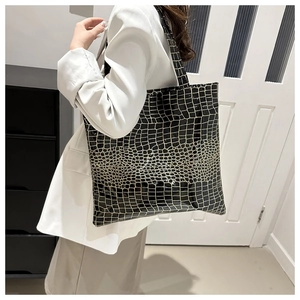 Model wearing a large black tote bag with glossy gold crocodile pattern texture