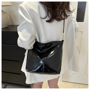 Detail of glossy black patent leather tote bag with elegant black and gold chain strap