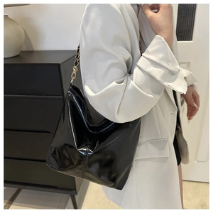 Glossy black patent leather bucket bag with gold chain strap on white blazer