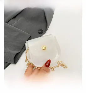 Détail du sac selle blanc translucide avec bandoulière chaîne dorée sur blazer gris