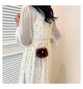 Détail d'un mini sac bandoulière marron translucide avec boucle dorée sur robe blanche