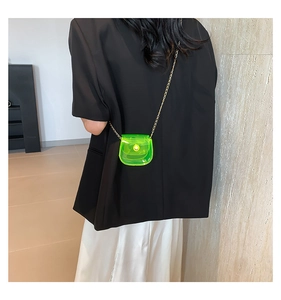 Mini sac bandoulière transparent vert néon avec chaîne dorée sur un blazer noir