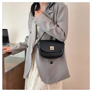 Détail d'un sac besace noir mat avec un fermoir doré porté par un mannequin