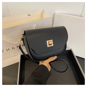 Gros plan d'un sac besace en cuir noir avec boucle dorée posé sur une boîte blanche