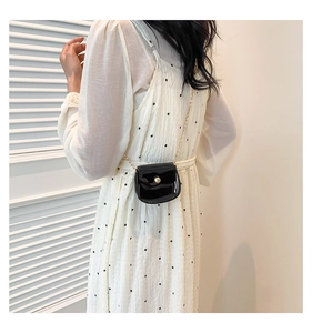 Petit sac bandoulière chic en cuir verni noir avec chaîne dorée sur une robe blanche