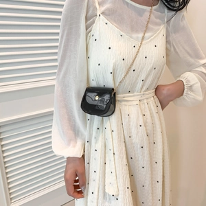 Mini sac bandoulière noir brillant avec chaîne dorée sur robe à pois élégante