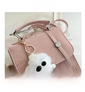 Close-up of pink litchi grain leather bag with plush white pendant and silver buckle
