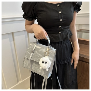 Detail view of silver grey textured handbag with plush doll charm and metallic lock closure