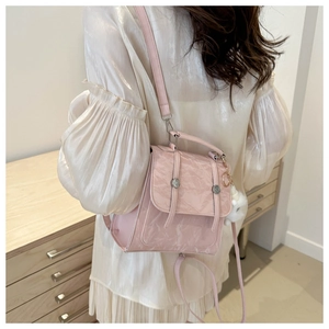 Detailed back view of a pink textured backpack with silver buckles and a white pompom charm