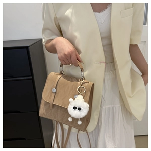 Detail of pleated khaki crossbody bag featuring a plush monster charm and top handle