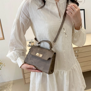 Brown suede crossbody bag with gold twist lock shown in a stylish home setting
