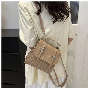 Detail of tan wrinkled leather handbag featuring silver round buckles and top handle