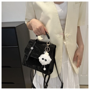 Detail of black embossed crossbody bag with plush charm on a beige blazer outfit
