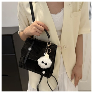Detail of black textured leather shoulder bag with plush monster charm and silver buckle