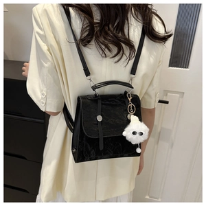 Detail of black pleated faux leather backpack with cute white plush monster charm