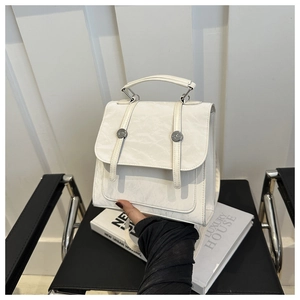 Detail of cream pleated leather handbag featuring decorative straps and metal buckles