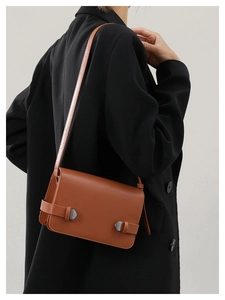 Borsa a tracolla in pelle marrone con fibbie argento indossata su un blazer nero elegante