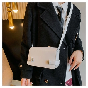 Dettaglio della borsa a tracolla quadrata bianca minimalista con fibbie argentate su cappotto