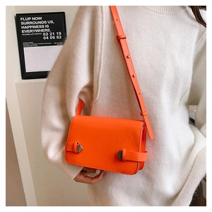 Dettaglio di una borsa a tracolla quadrata in pelle arancione su un dolcevita bianco